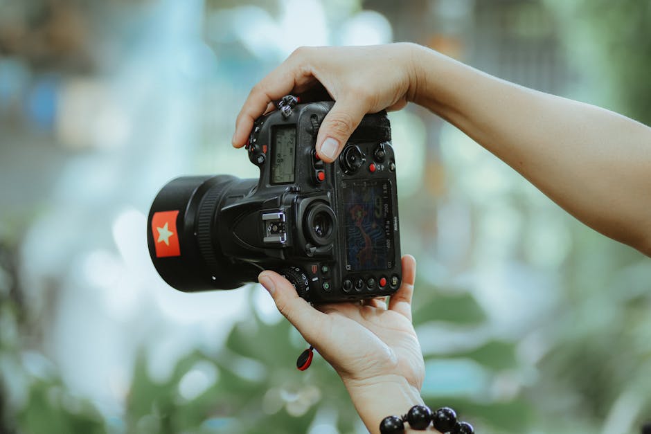 Hands holding a professional camera with nature in the background. Focus on camera details.