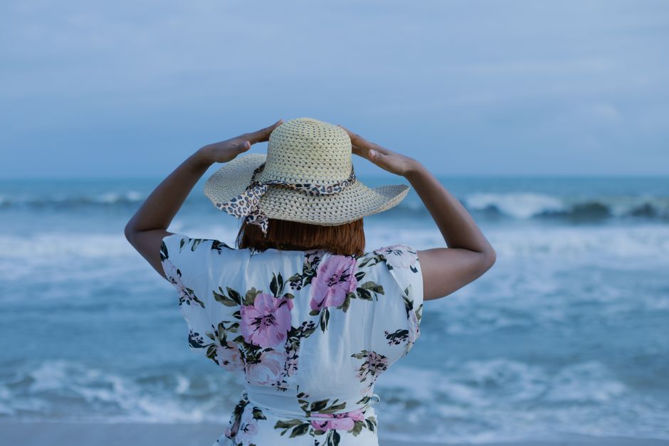 Woman enjoying a peaceful day at the tropical beach, wearing a sun hat and floral dress.