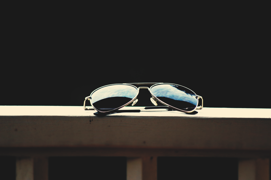 A close-up of aviator sunglasses reflecting the sky, set against a dark background.