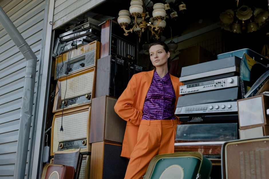 Woman in vibrant outfit posing with vintage audio equipment at an outdoor flea market.
