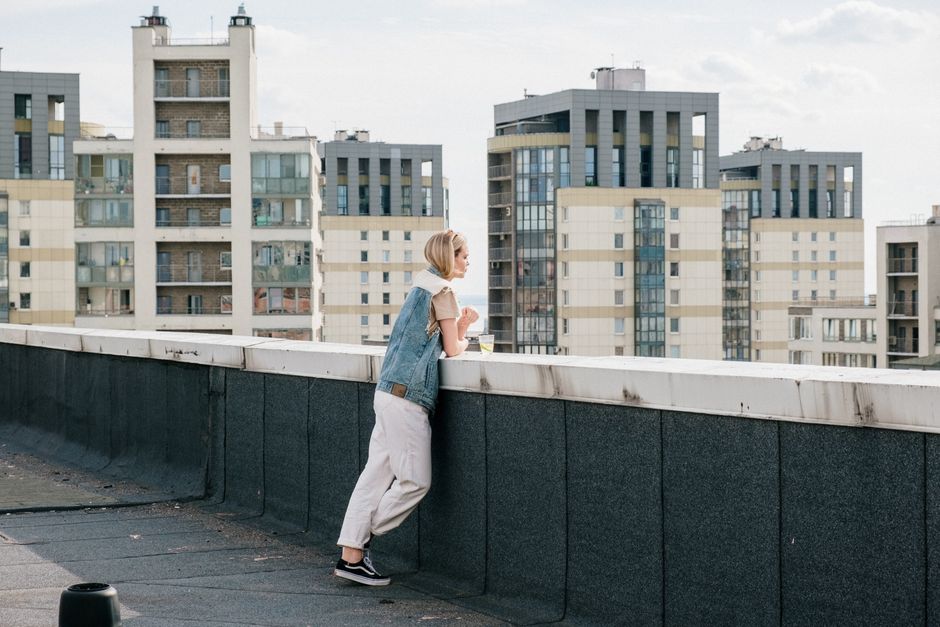 A woman on a rooftop, overlooking urban residential buildings on a sunny day.