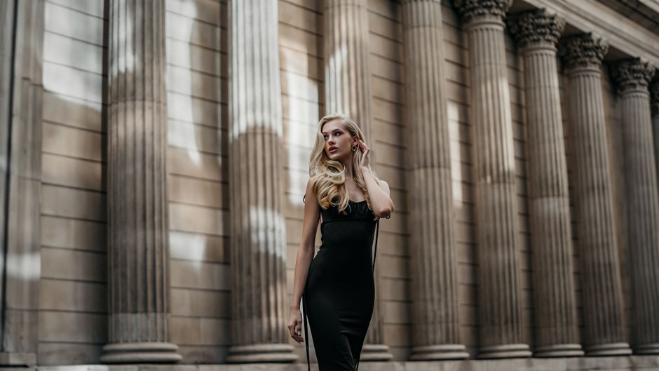 Striking fashion photography capturing a blonde woman in a black dress posing by classic colonnades.