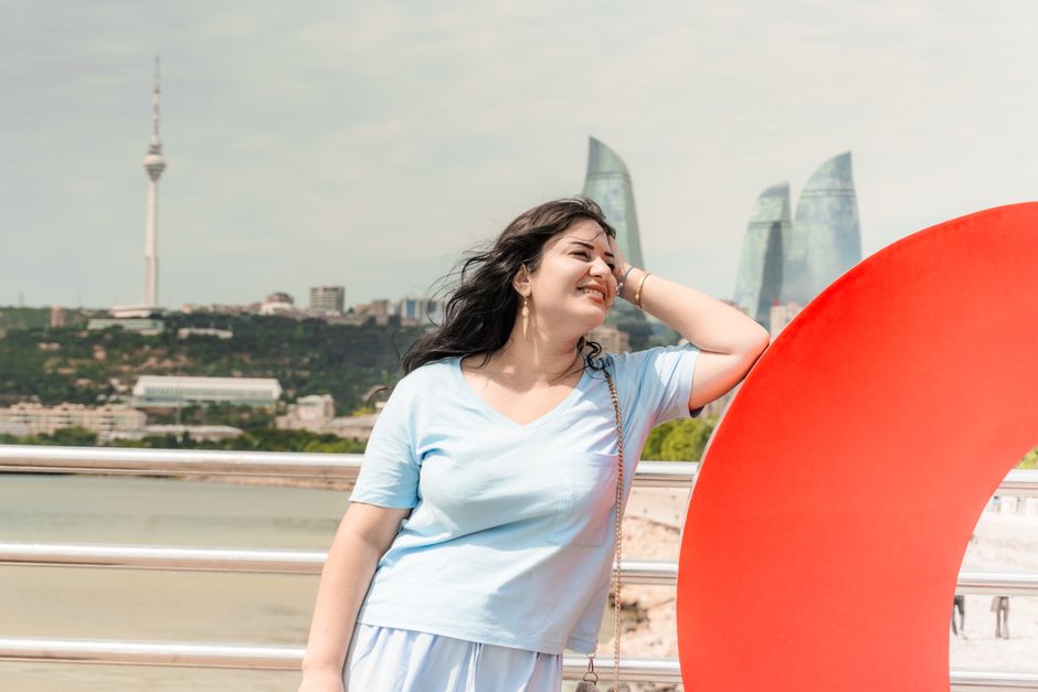 Happy woman in Baku with Flame Towers and TV Tower in background, enjoying a sunny day.