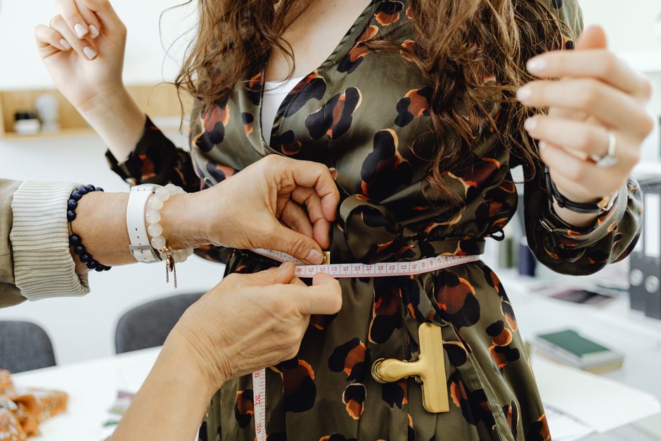 Close-up of a fashion designer measuring a dress with tape for precise fitting.
