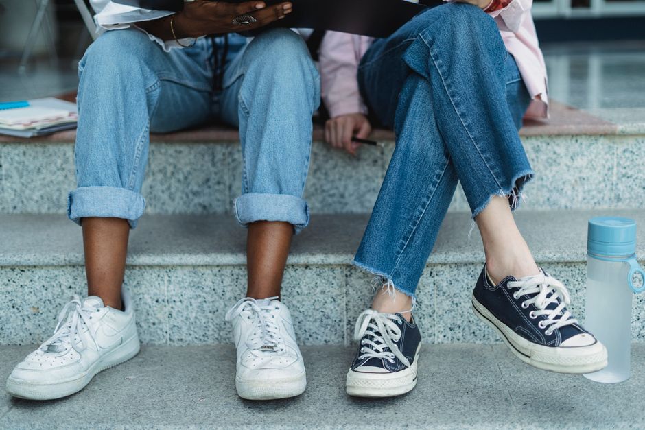 Crop anonymous diverse girlfriends in casual denim wear studying together on stairs in city