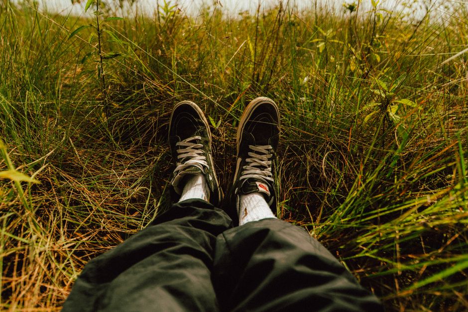 Person sitting in tall grass wearing sneakers, capturing a moment of relaxation and tranquility.
