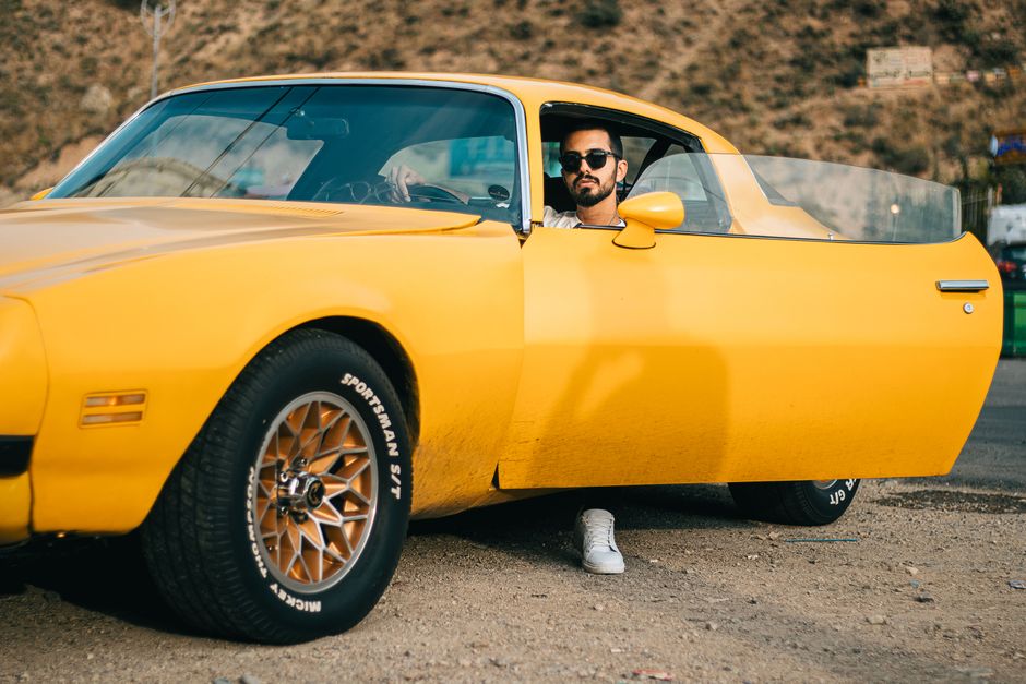 Man sitting inside a bright yellow vintage car with the door open, looking outdoors.