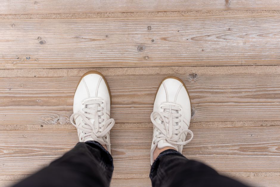 Aerial view of a person wearing white sneakers standing on wooden planks, showcasing casual fashion.