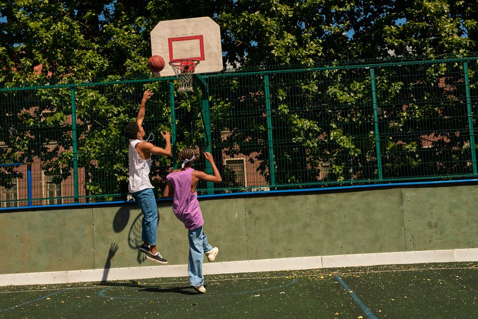 Dynamic outdoor basketball game with two teenagers jumping and shooting. Enjoying a sunny day.