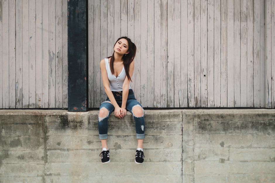 Teenage girl in casual outfit sitting on a concrete ledge in an urban setting.
