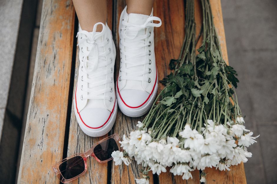 White high-top sneakers on wooden bench with sunglasses and daisies. Stylish and casual vibe.