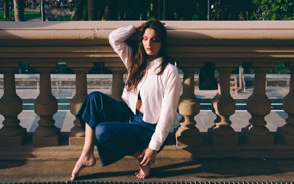 A young woman in a white jacket sitting contemplatively outdoors against a balustrade.
