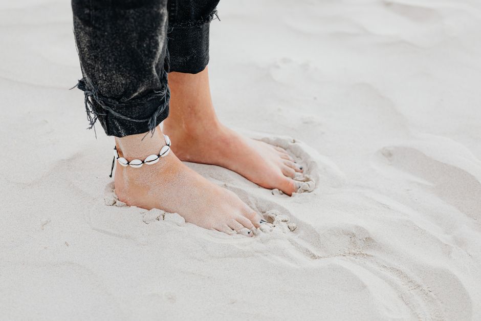 Close-up of feet on sandy beach wearing anklet. Relaxed summer vibe.