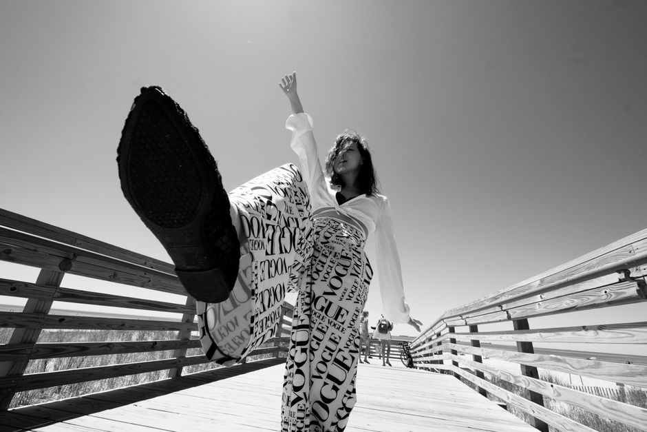 A fashionable woman poses on a boardwalk, showcasing her Vogue print pants in a dynamic monochrome shot.