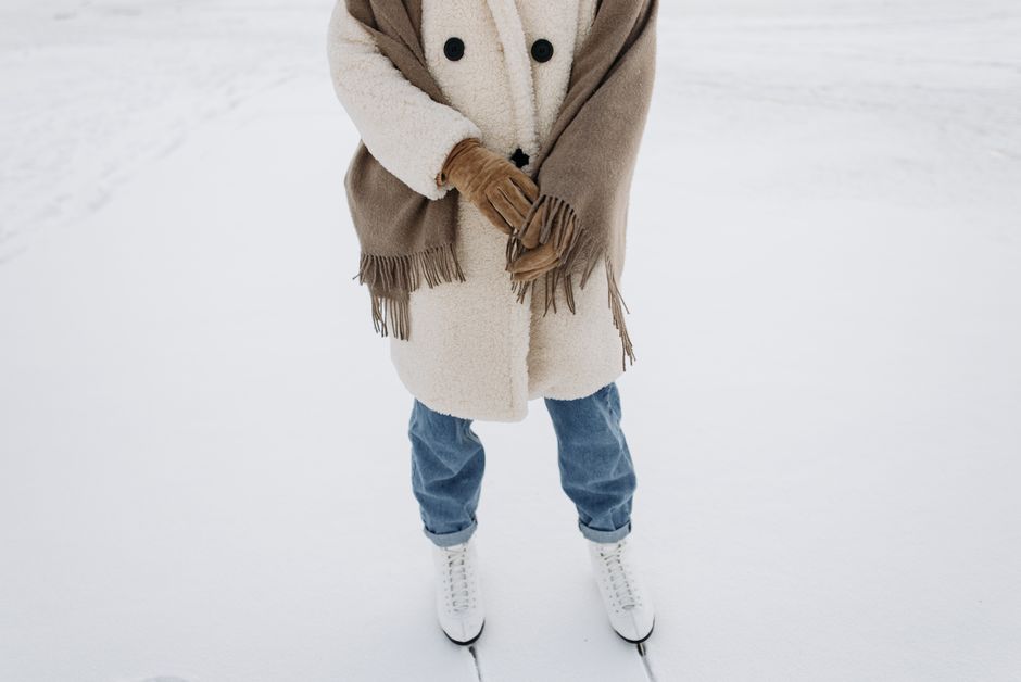 Woman in warm coat and gloves standing on snow-covered ground in winter.