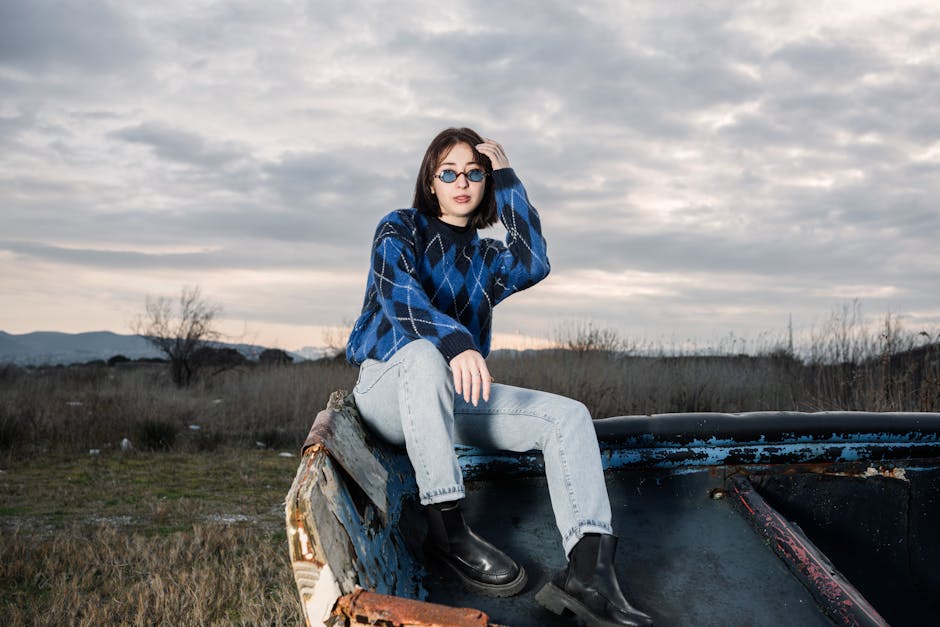 A person in a blue sweater and jeans poses outdoors in an open field.